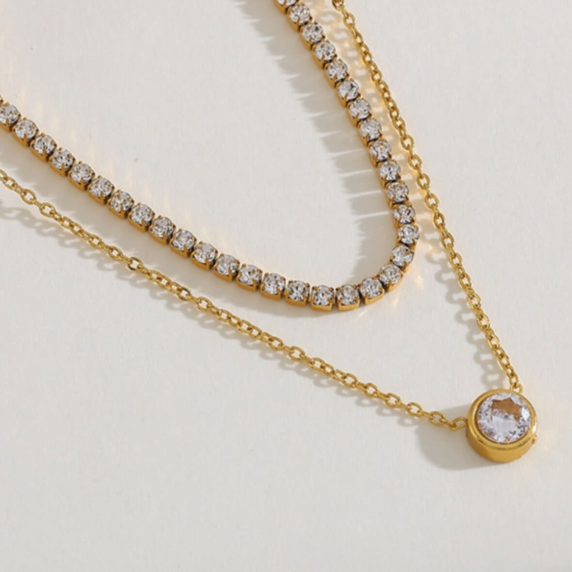 Gold layered tennis necklace closeup with pavé links and round pendant with clear stone
