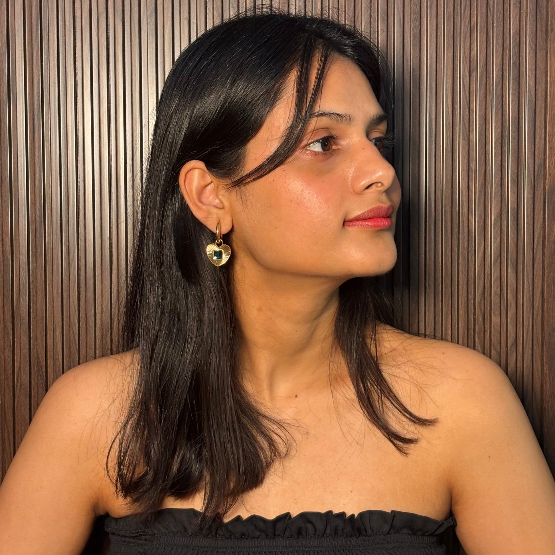 Gold hoop earrings with heart pendant and green square gemstone on model