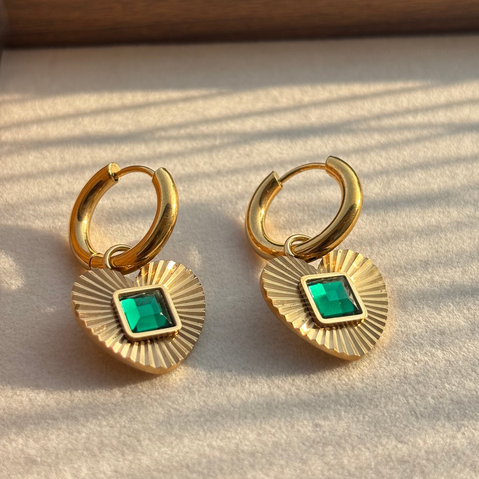 Gold hoop earrings with heart pendant and green square gemstone detail