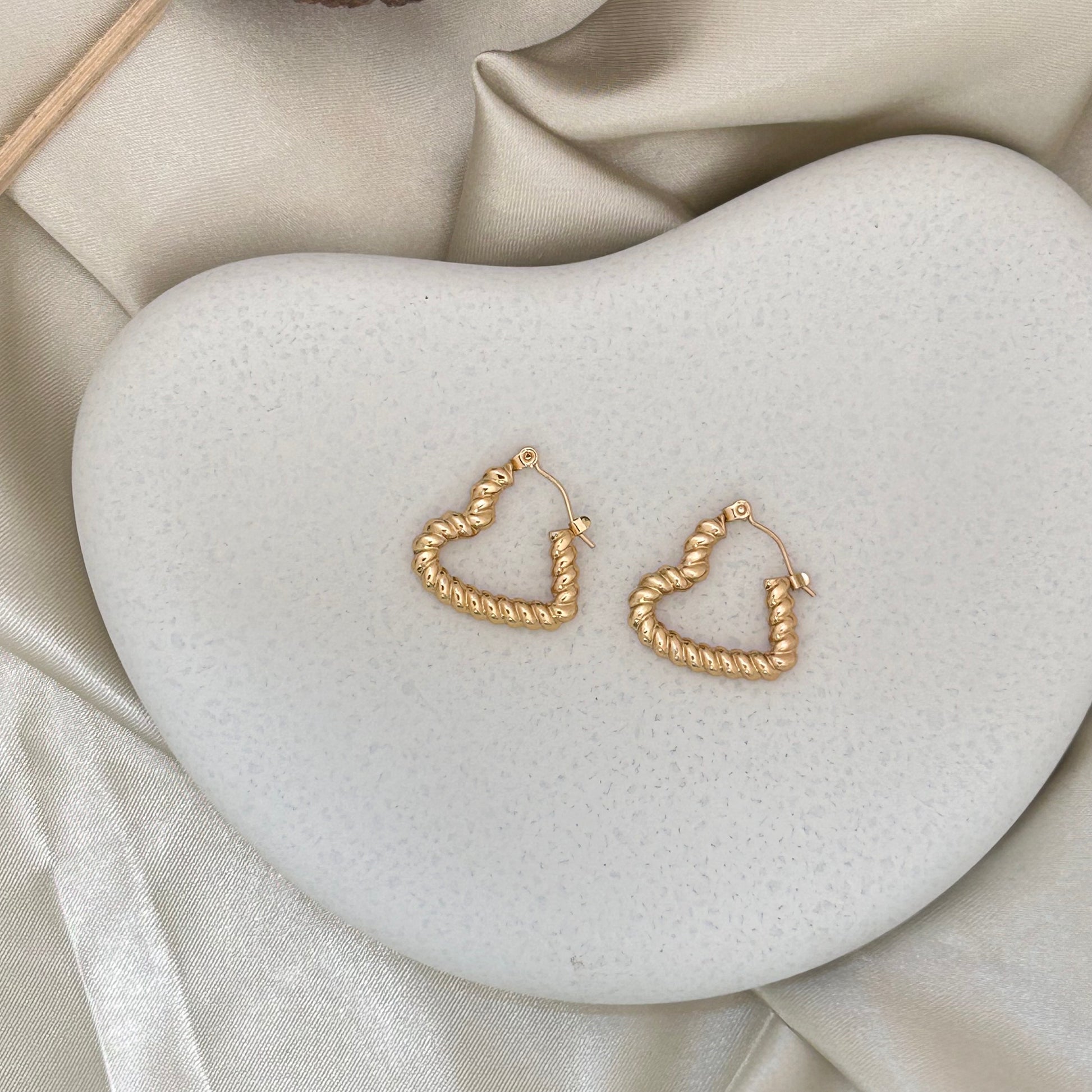 Gold-tone heart wrap hoop earrings on a white heart-shaped display