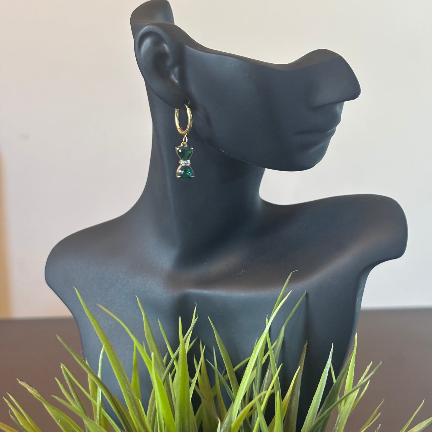 Gold hoop earrings with green bow-shaped drop stones, dangling