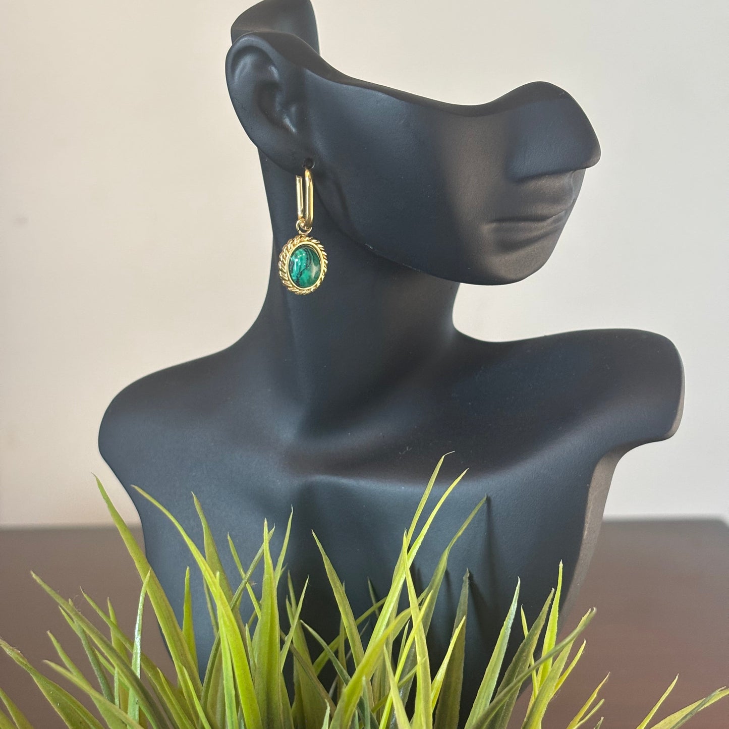 Gold-tone drop earrings with green oval stone, hanging from hinged hoops on a mannequin