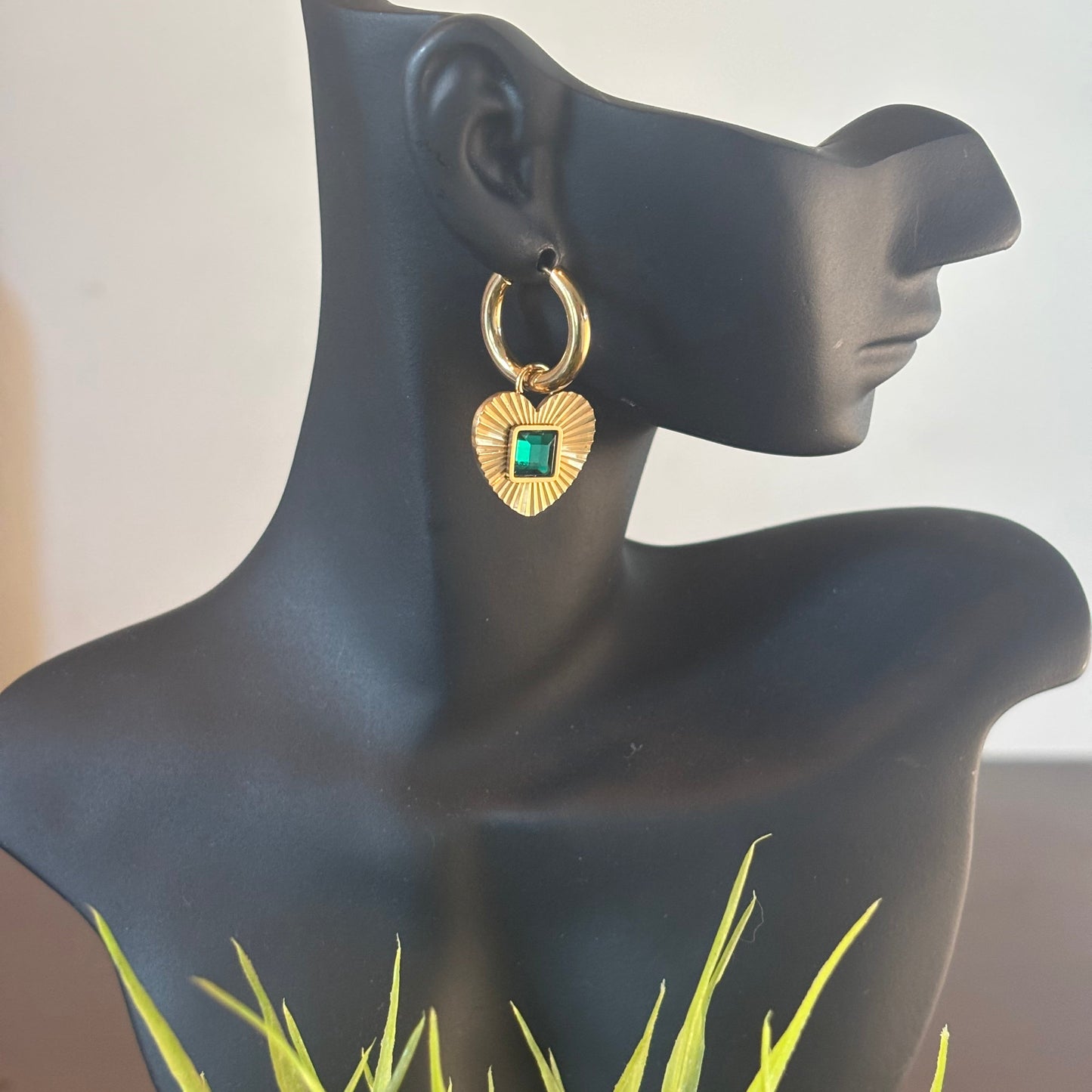 Gold hoop earrings with heart charm and green square gemstone, profile view