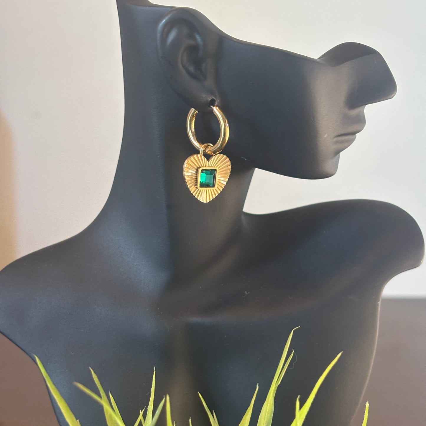 Gold hoop earrings with heart charm and green square gemstone, side view