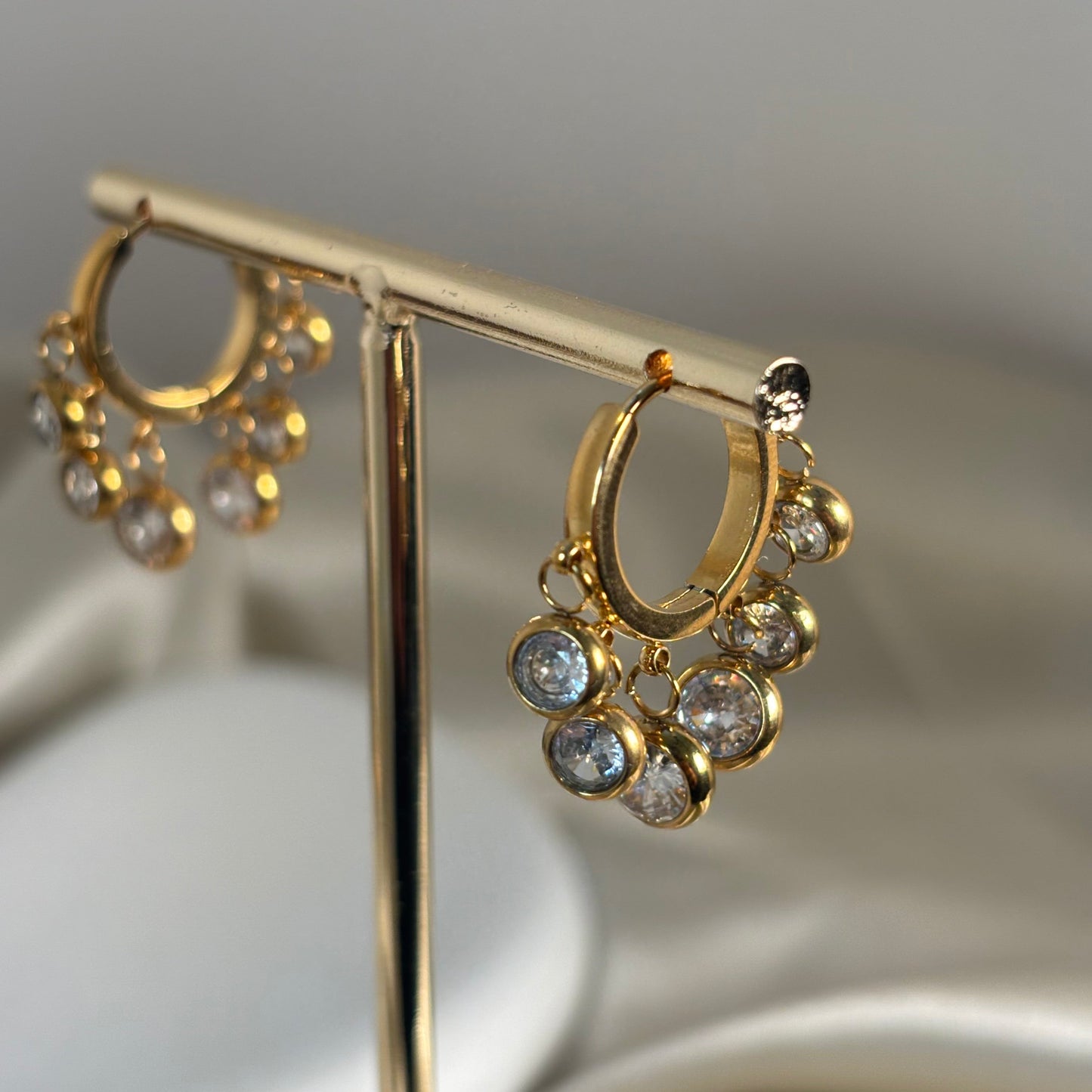 Gold-tone hoop earring with dangling round crystals and small charm drops