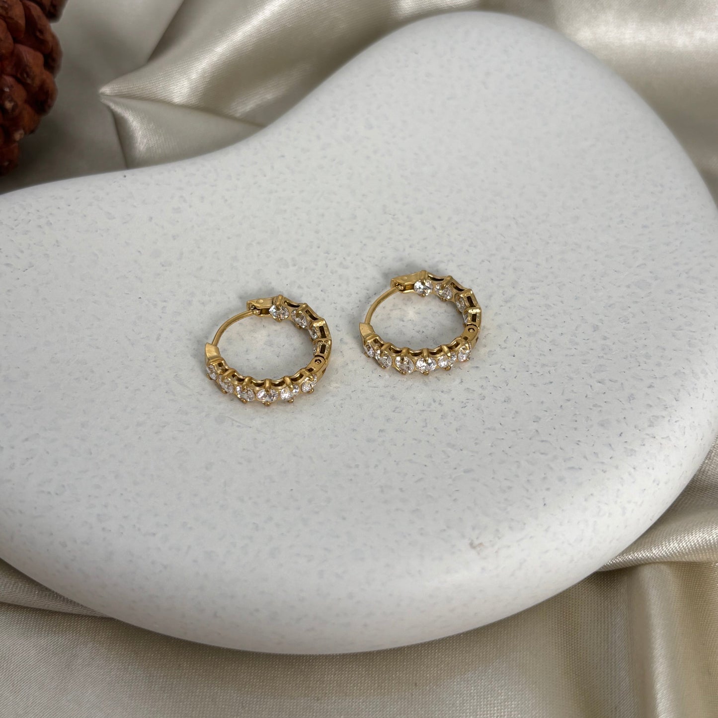 Gold hoop earrings with clear pavé stones, separate pair view on a white cushion