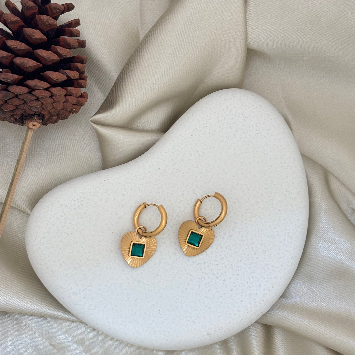 Gold hoop earrings with heart pendant and green square gemstone on display