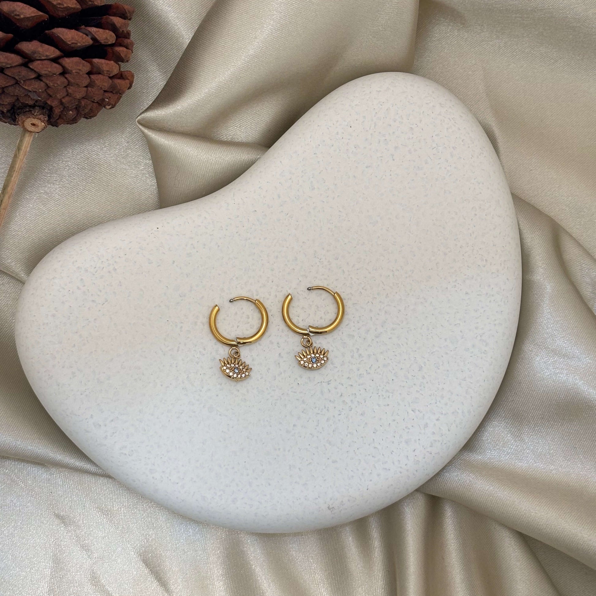 Gold huggie hoop earrings with two round evil eye charms, blue center details