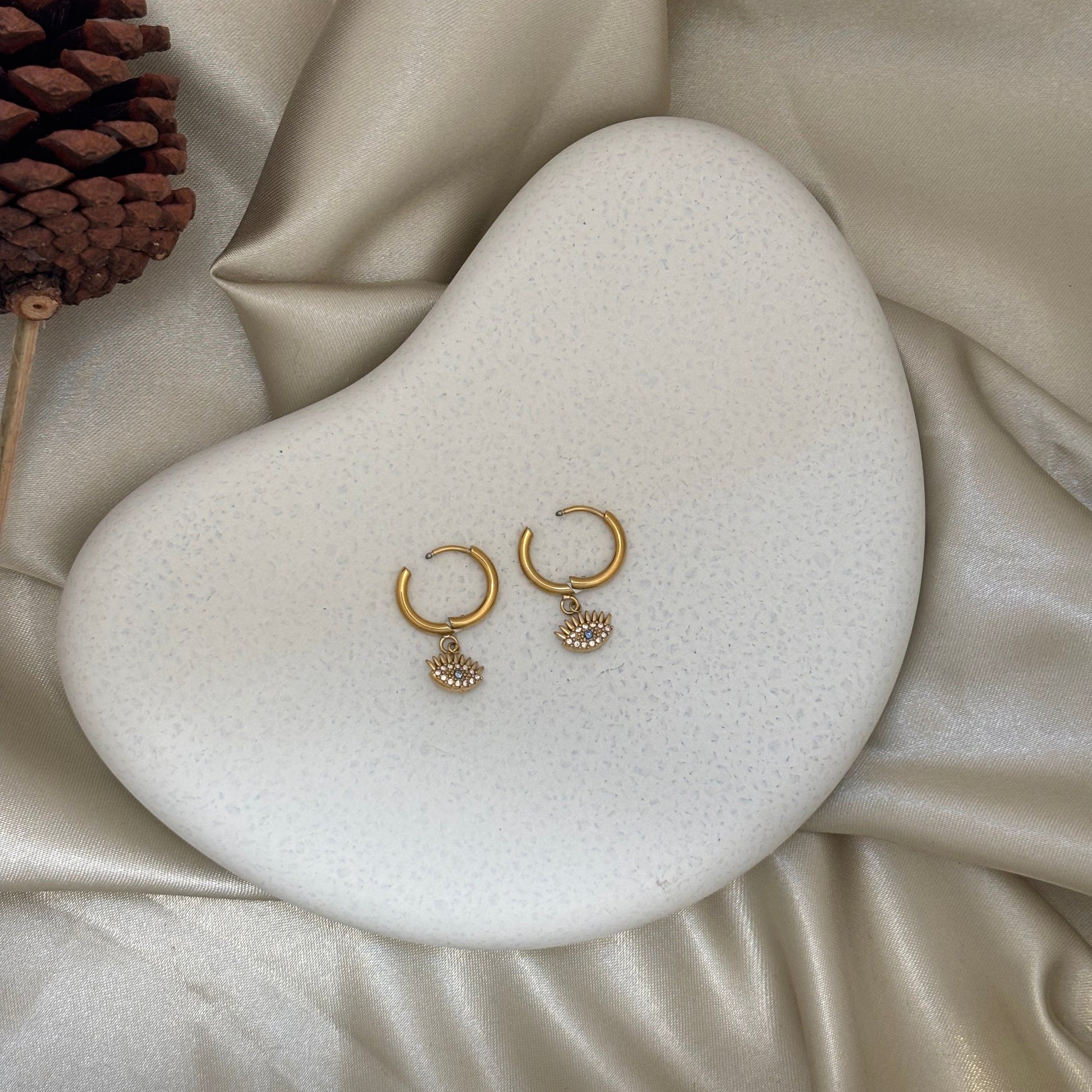 Gold huggie hoop earrings with two evil eye charm drops, blue centers on both hoops
